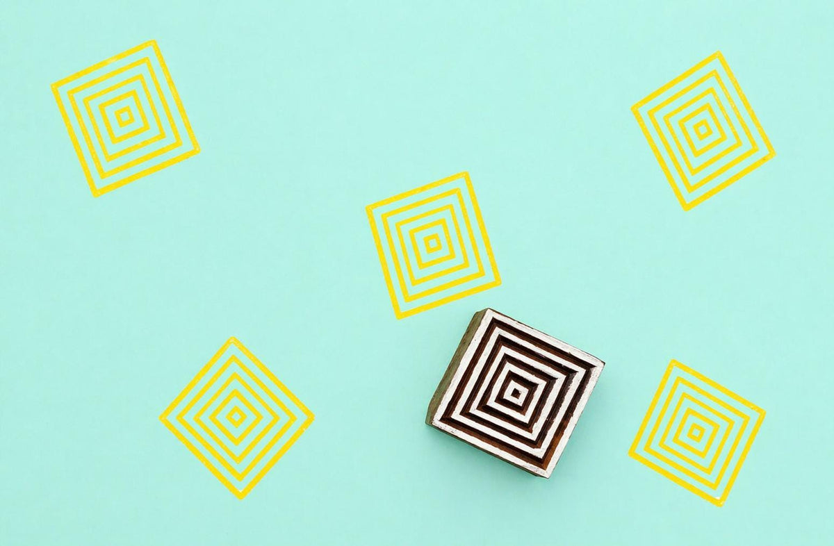 Hand carved wooden block stamp creating a repeating geometric square pattern with concentric lines in yellow ink