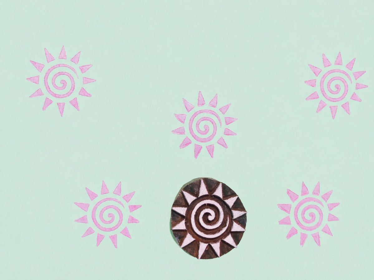 Sun design wooden printing block creating circular pattern on paper