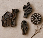 Hand carved wooden printing block set with camel, cactus and sun designs on neutral background