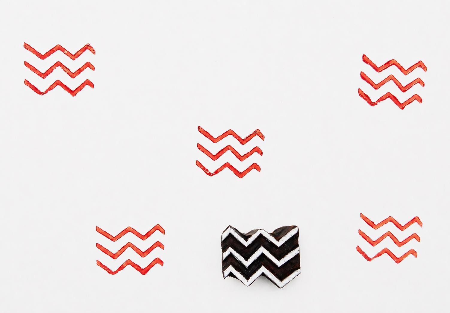 Hand-carved wooden zigzag stamp with red ink pattern printed on white background