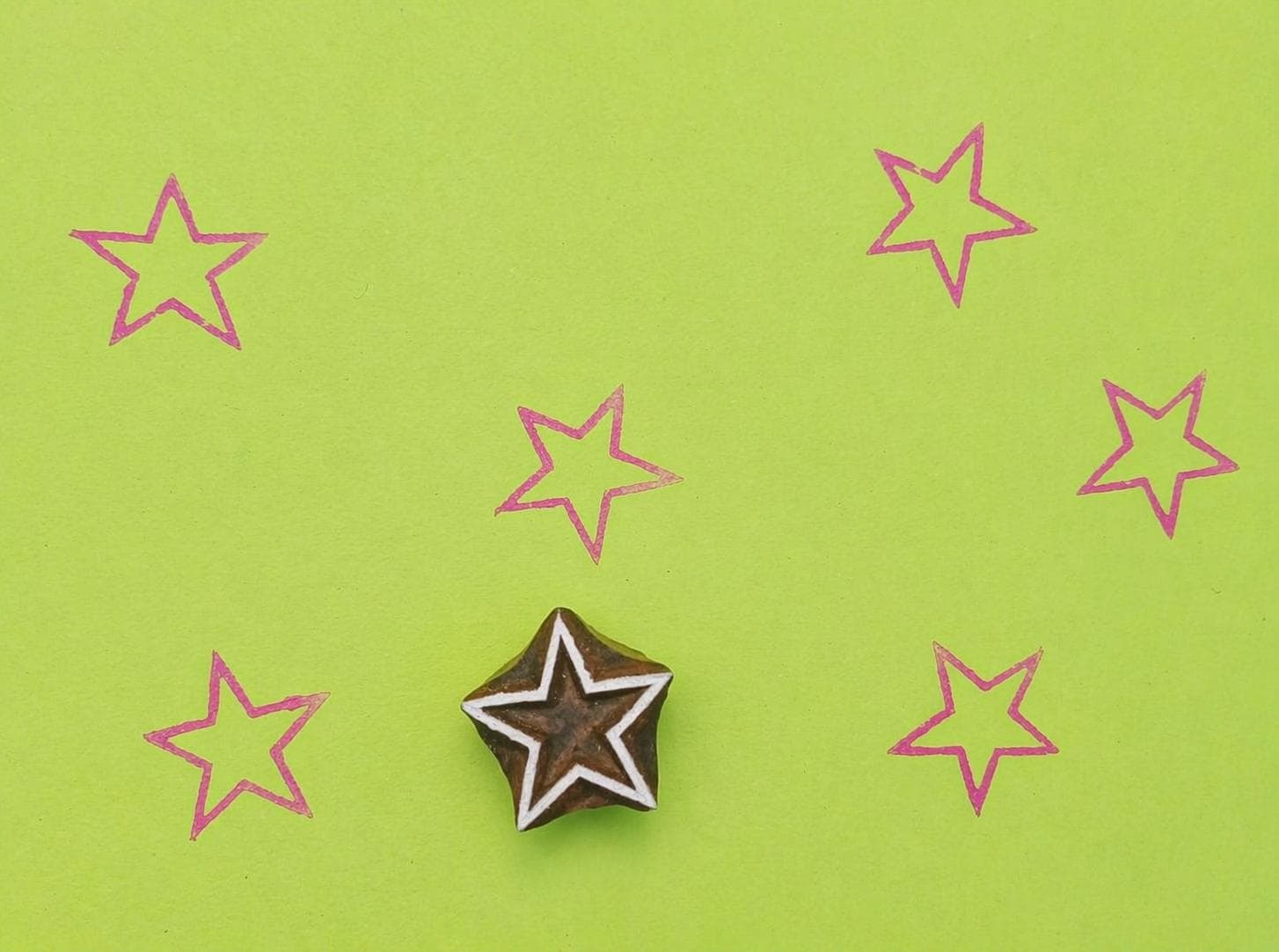 Star shaped wooden block stamp with repeated pink star prints on green background