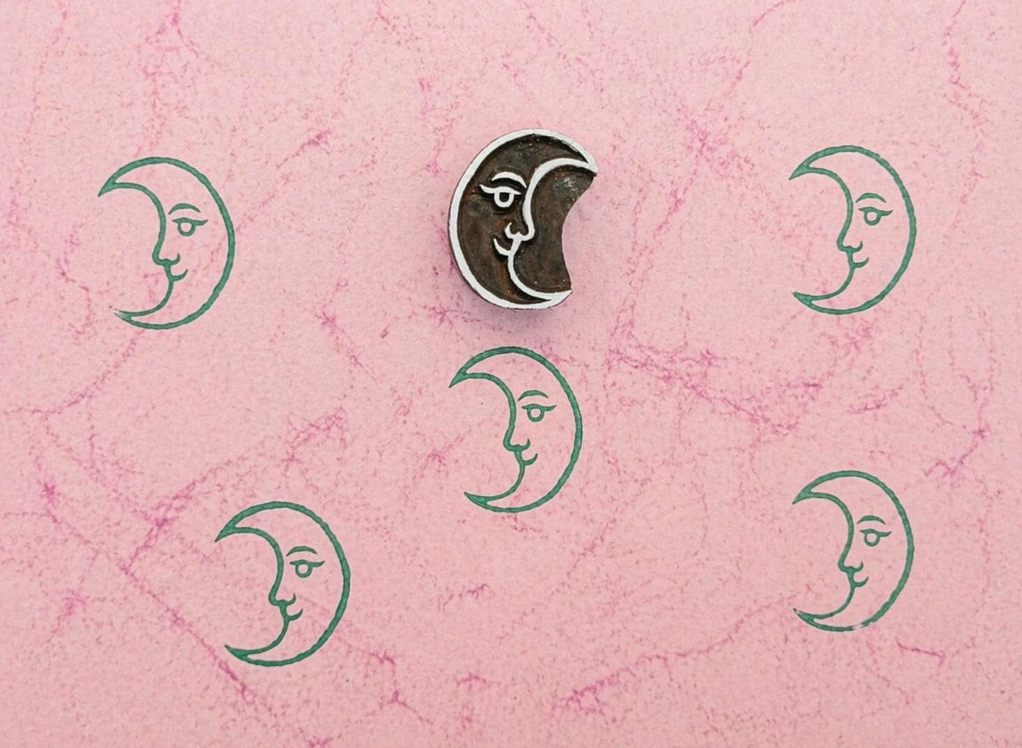 Crescent moon wooden stamp with repeating green moon prints on textured pink paper
