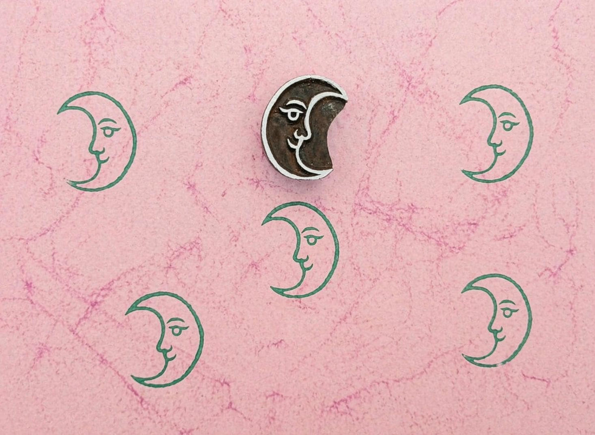 Crescent moon wooden stamp with repeating green moon prints on textured pink paper