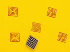 Concentric square wooden stamp creating repeating orange geometric pattern on yellow background