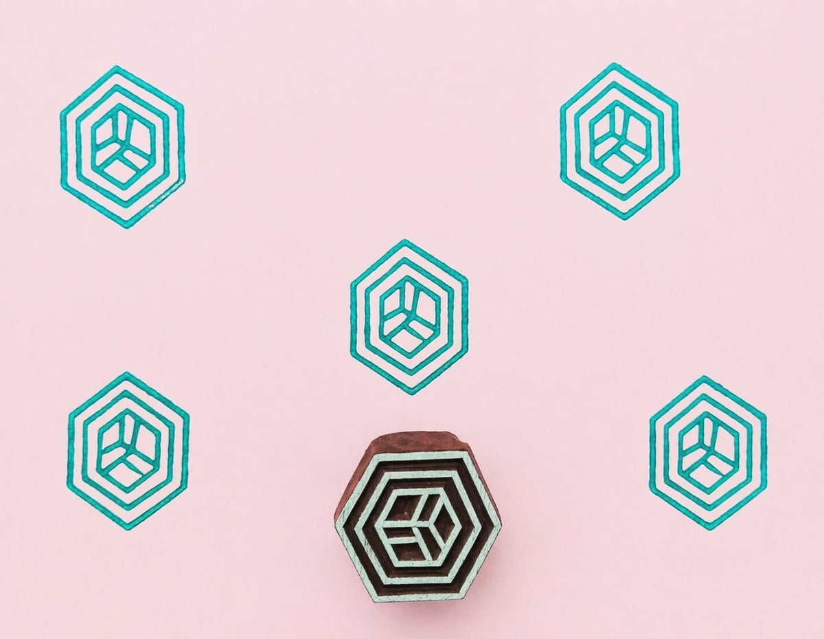 Hexagon prism wooden stamp printing teal geometric pattern on soft pink paper