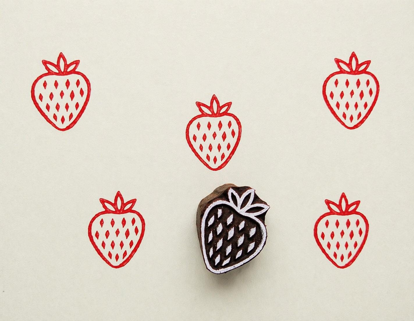 Hand carved wooden printing block with a simple strawberry illustration for fabric printing, paper crafts, and repeat fruit patterns.