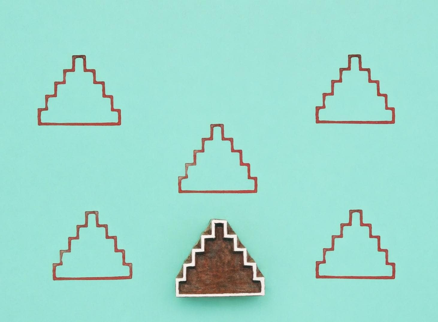 Wooden block stamp with step pyramid design shown with repeated printed pattern on teal background