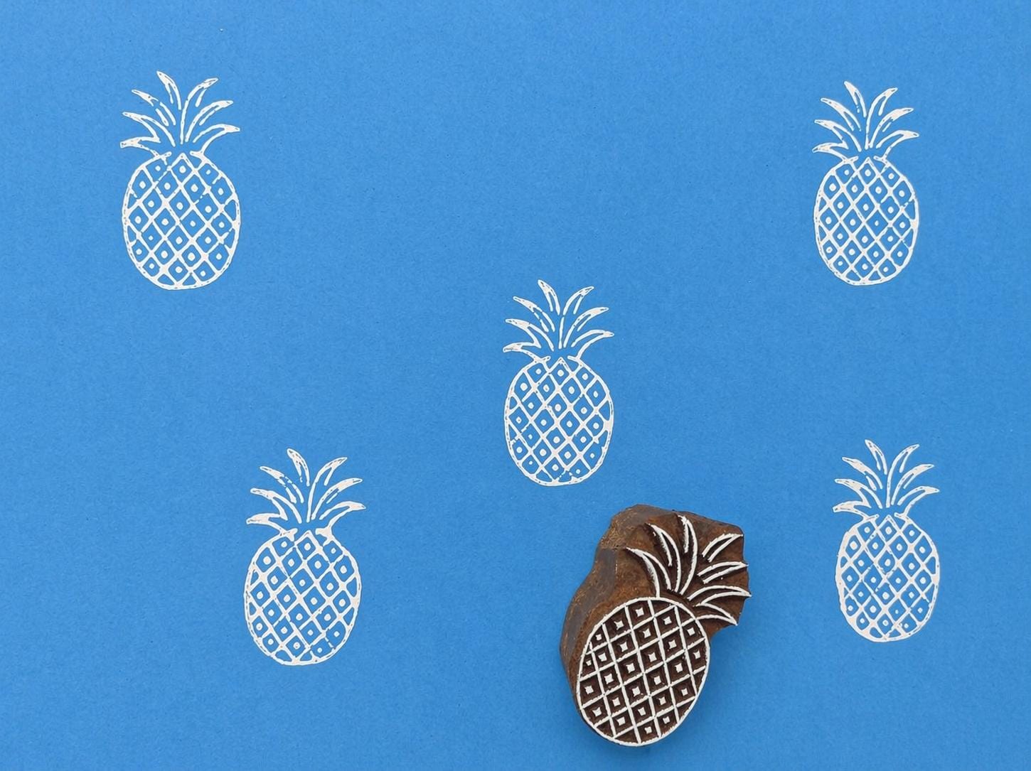 Pineapple wood block stamp with repeating print pattern on blue background