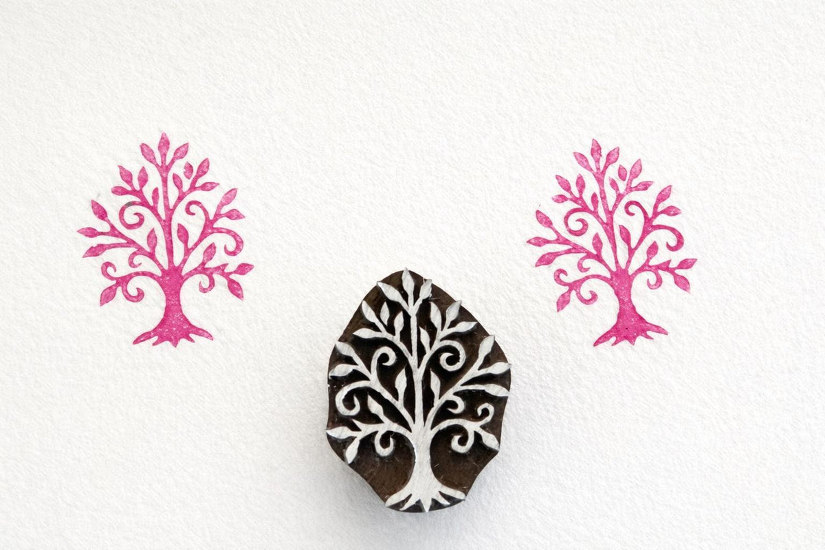 Hand carved wooden tree stamp with swirling ornamental branches printed in pink ink on white paper