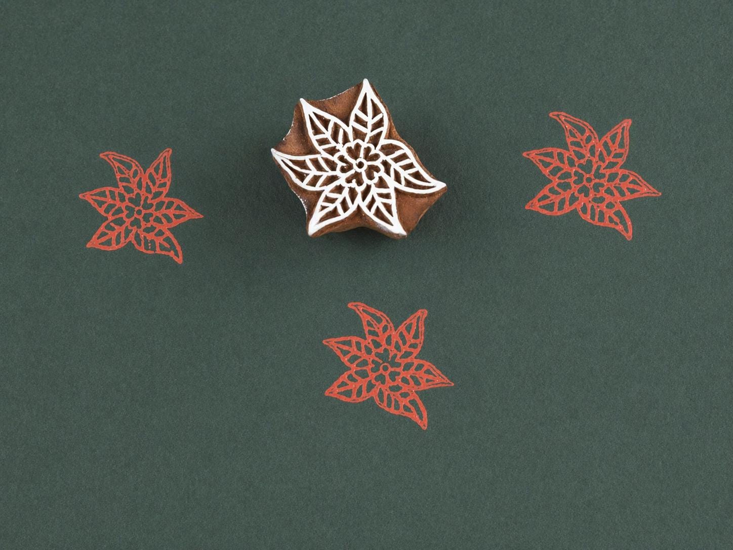 Hand carved wooden poinsettia block stamp printing intricate lace floral star pattern in red ink on dark green paper