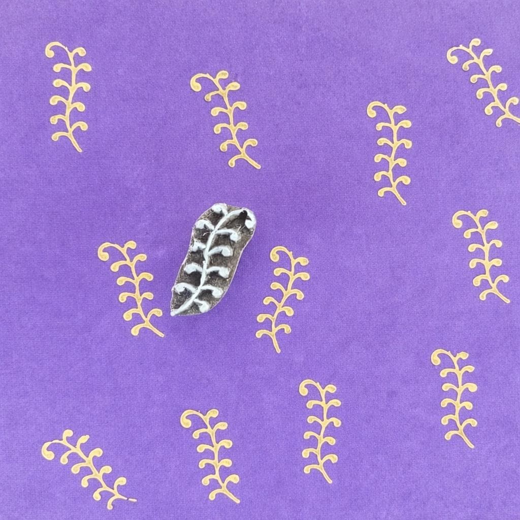 Hand carved Indian wooden printing block featuring small vine motif creating repeating yellow filler pattern on purple fabric