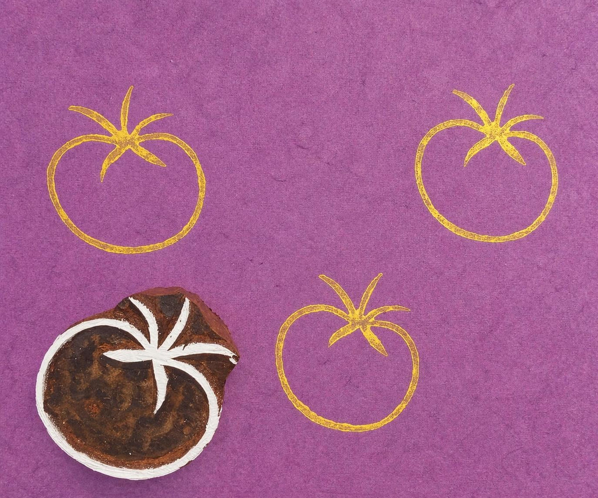 Hand carved tomato stamp creating repeating yellow prints on purple paper