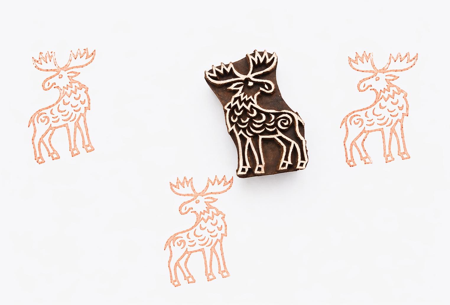 Hand carved wooden block stamp featuring a stylized moose design, used for printmaking on paper, fabric, or clay with repeated animal pattern impressions.