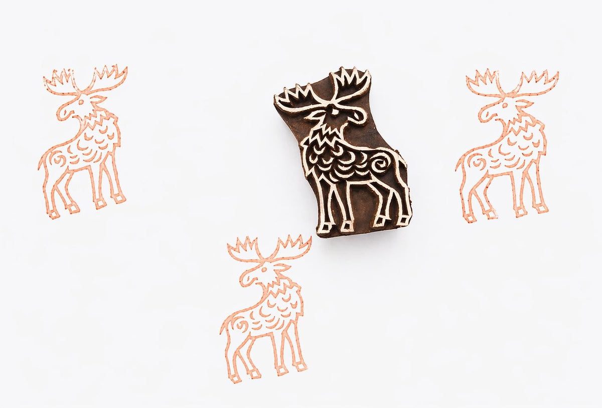 Hand carved wooden block stamp featuring a stylized moose design, used for printmaking on paper, fabric, or clay with repeated animal pattern impressions.