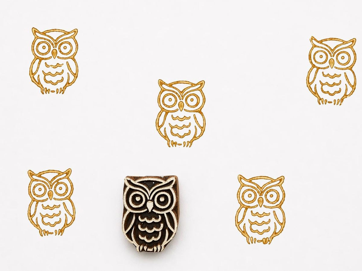 Hand carved wooden owl printing stamp with repeated golden owl impressions on white background, simple forest bird design for textile and craft printing