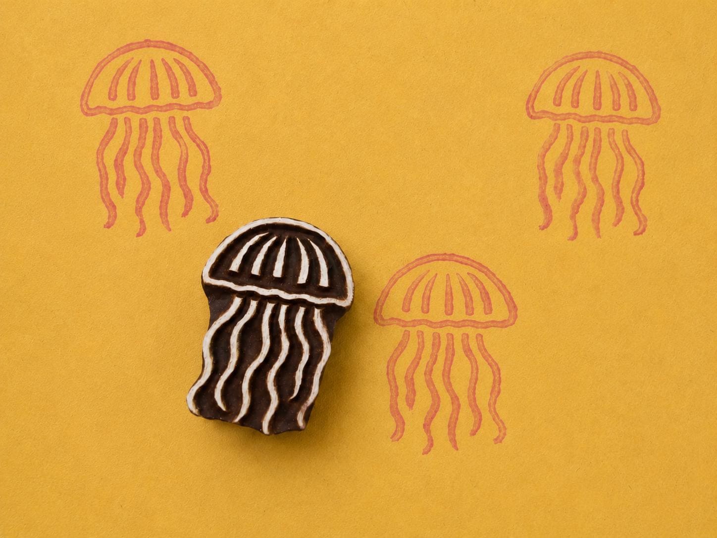 Hand carved wooden jellyfish block stamp printing flowing ocean jellyfish motif in coral ink on yellow background