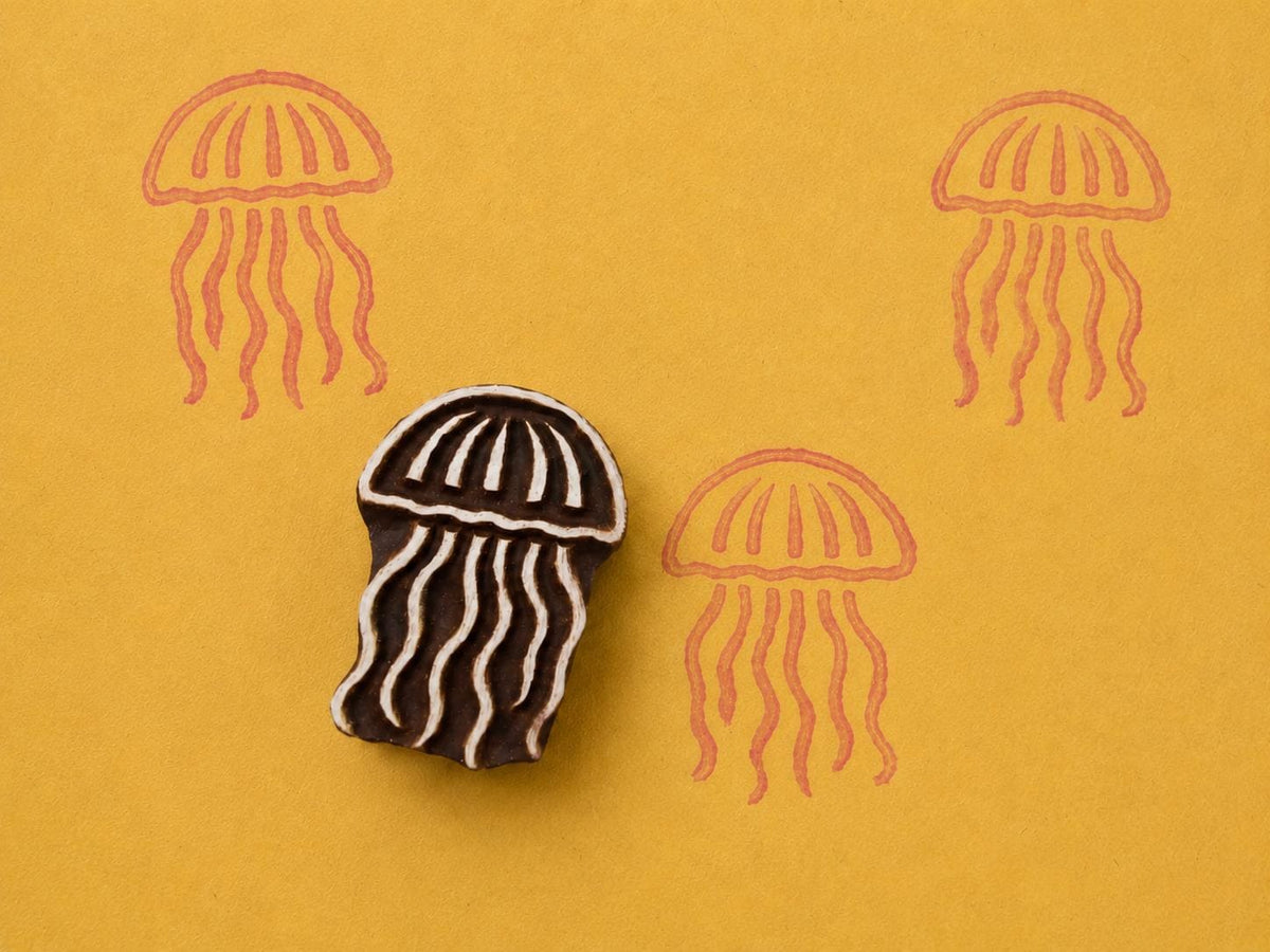 Hand carved wooden jellyfish block stamp printing flowing ocean jellyfish motif in coral ink on yellow background