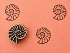 Hand carved wooden printing block featuring a coral fossil spiral shell motif stamped repeatedly on peach paper.