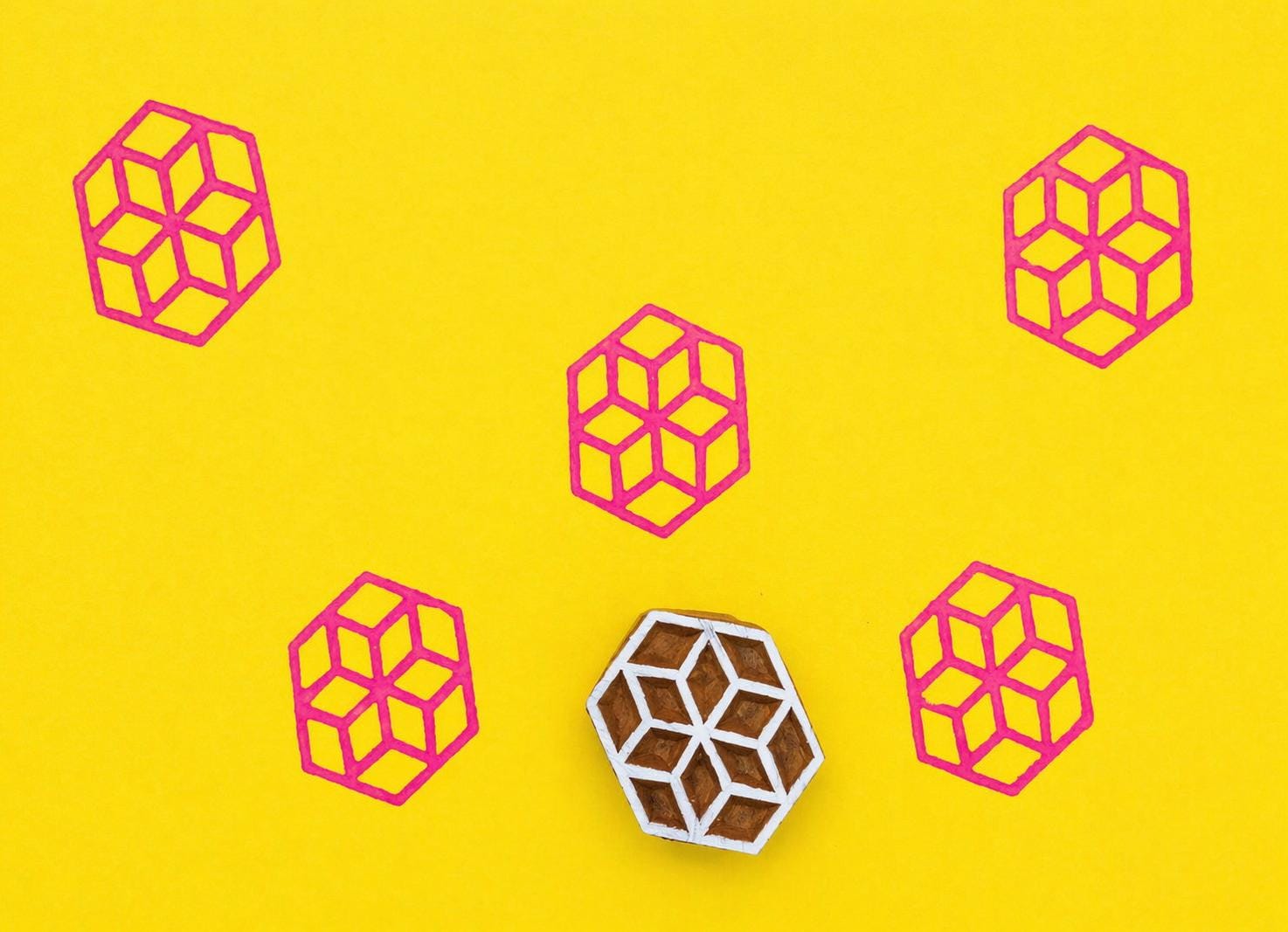Hand carved Indian wooden block with geometric cube design printed in pink on bright yellow background for textile, clay, pottery, and fabric printing.
