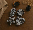 Set of hand carved wooden printing blocks featuring fish, jellyfish, seashell, and starfish designs for coastal fabric printing and ocean themed craft projects.