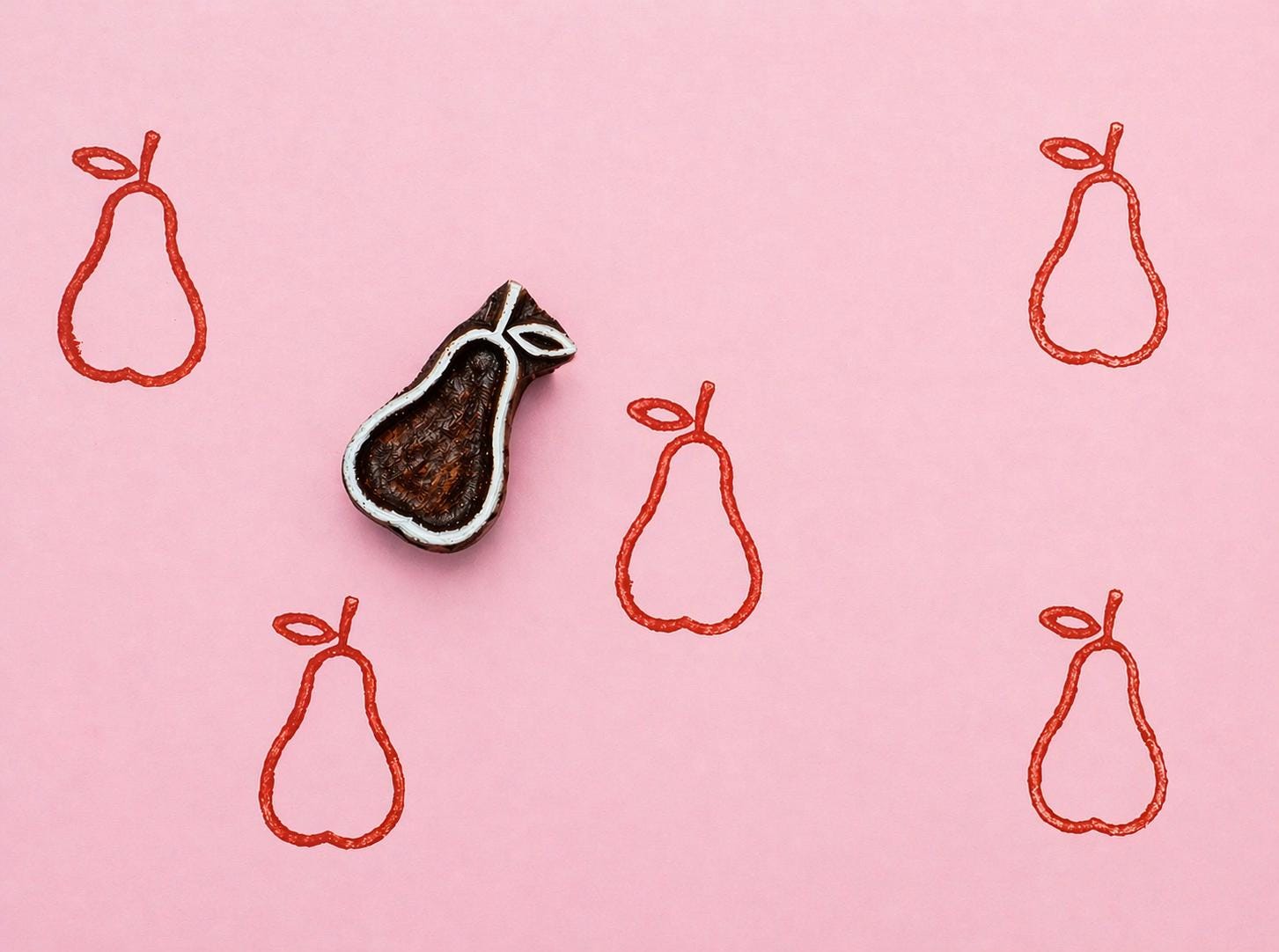 Hand carved wooden pear block stamp printing minimalist fruit pattern in red ink on pink background