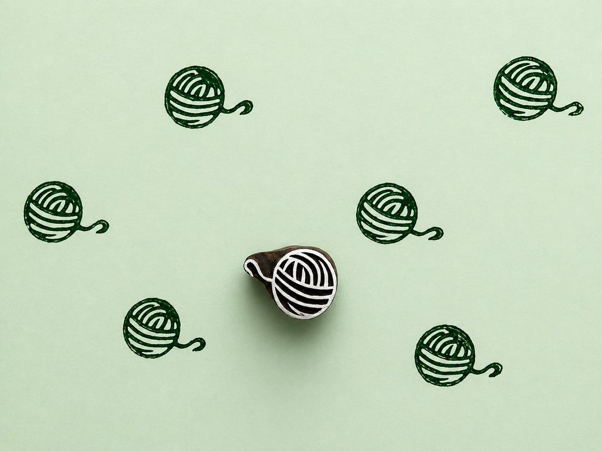 Indian wooden printing block with yarn ball motif stamped in green for knitting, crochet, and textile craft projects.