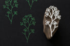 Hand carved wooden printing block featuring a delicate clover vine botanical motif stamped in green ink on dark textured paper.