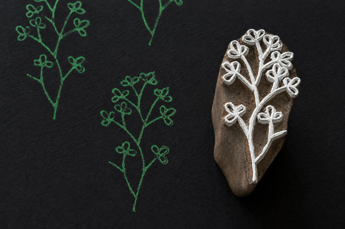 Hand carved wooden printing block featuring a delicate clover vine botanical motif stamped in green ink on dark textured paper.