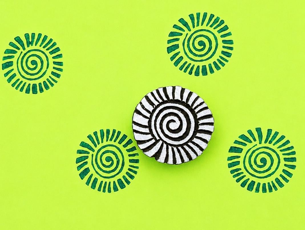 Hand carved wooden printing block with a tribal spiral sunburst motif for geometric textile printing and repeat surface patterns.