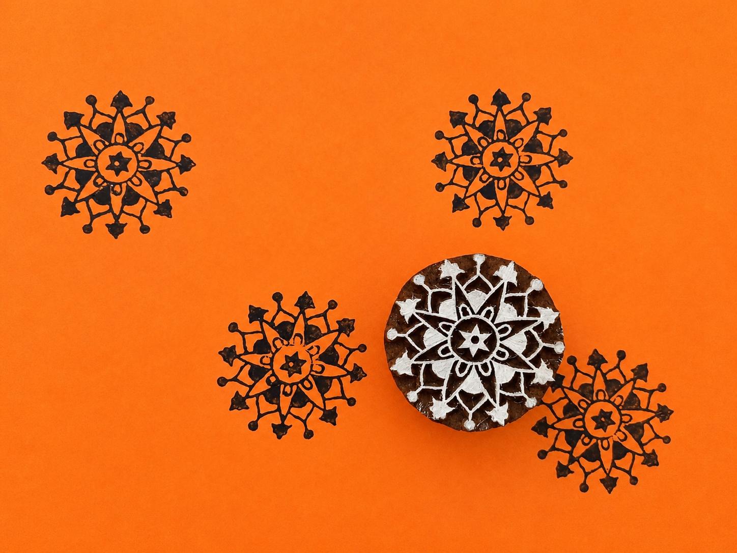 Hand carved wooden rosette compass block stamp printing intricate radial folk motif in black ink on orange background