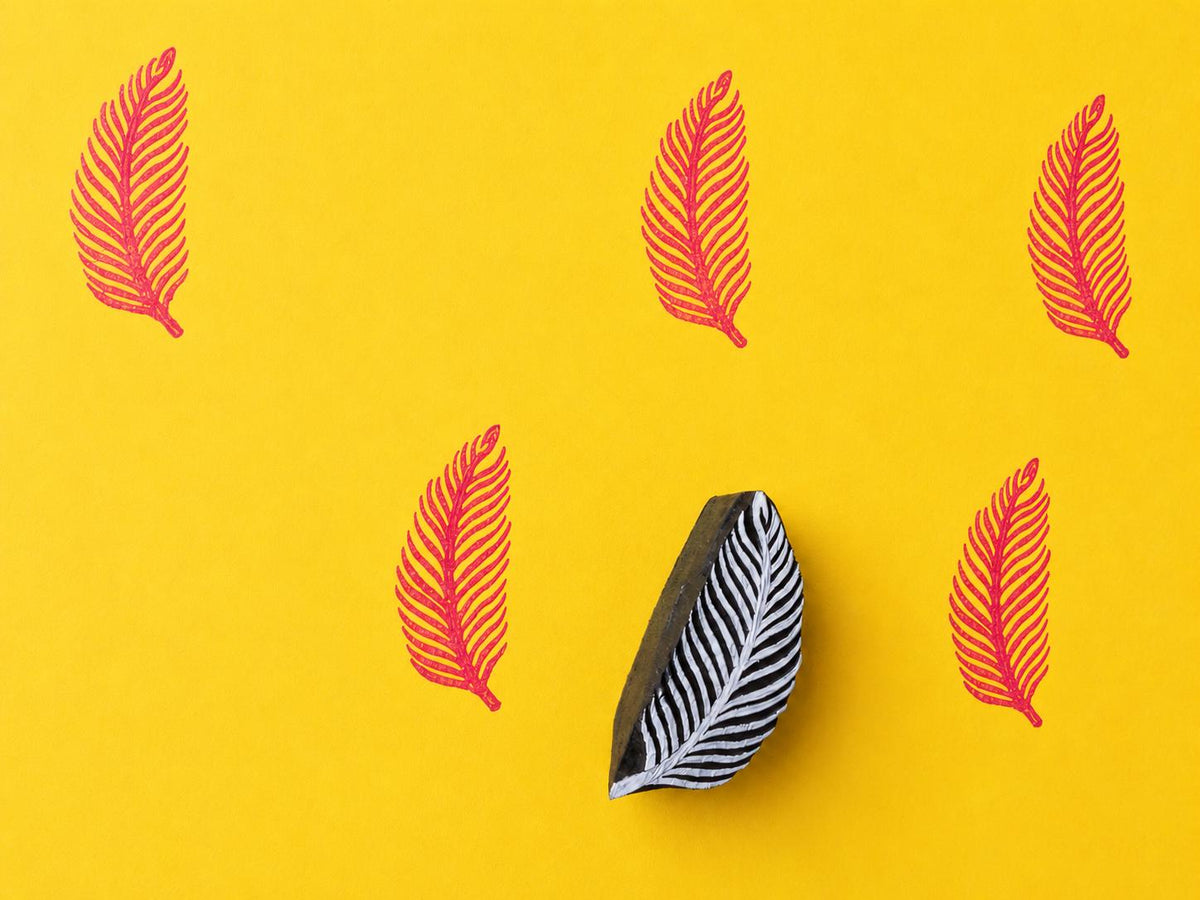Hand carved wooden tropical frond block stamp printing delicate feather leaf motif in pink ink on yellow background