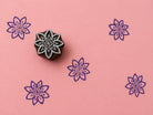 Hand carved Indian wooden block with geometric star flower motif printed in purple on pink background for fabric printing, pottery, clay, and paper crafts.