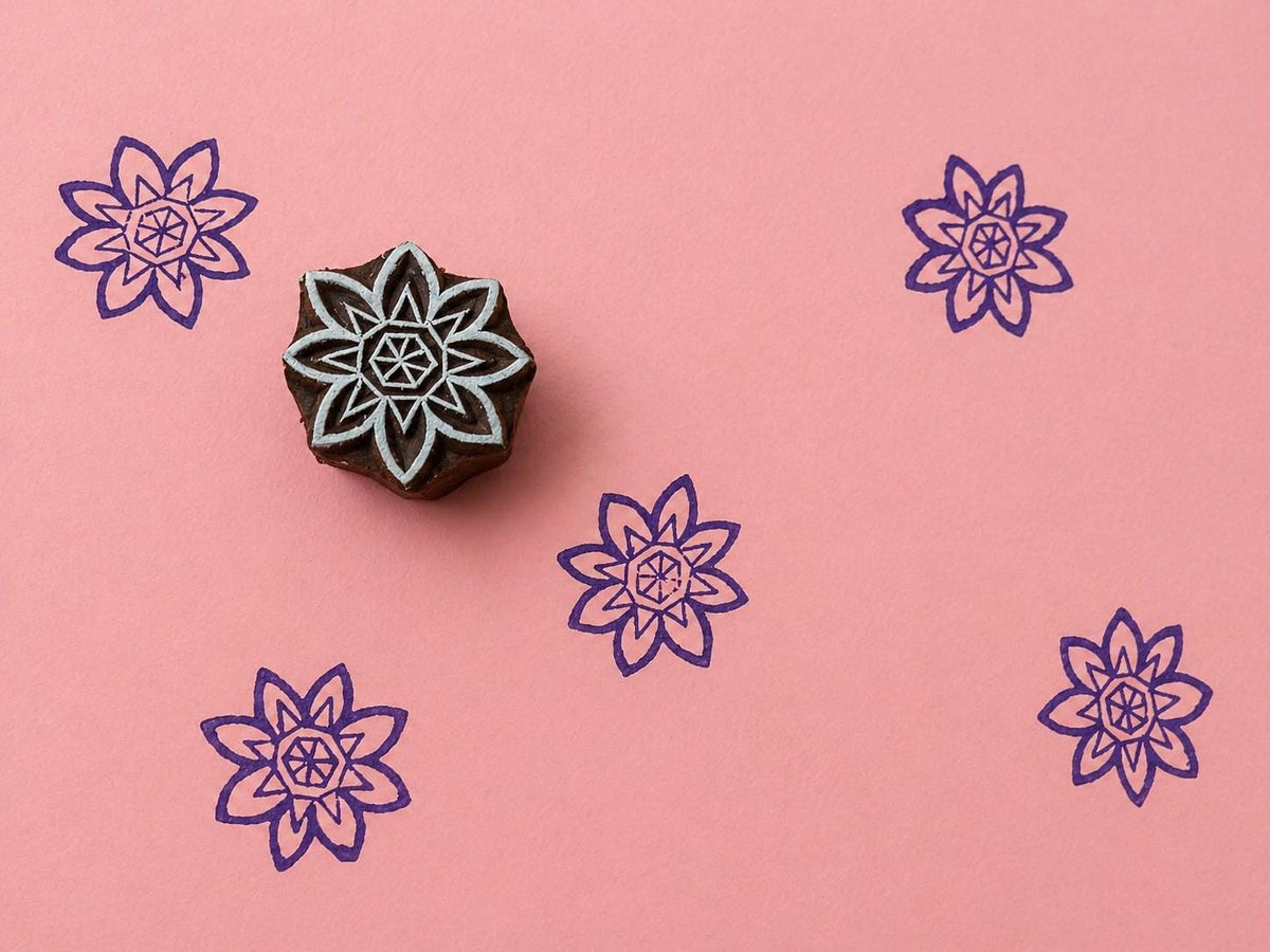 Hand carved Indian wooden block with geometric star flower motif printed in purple on pink background for fabric printing, pottery, clay, and paper crafts.