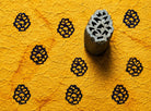 Hand carved pinecone wood block stamp printed repeatedly on textured handmade yellow paper with woodland folk motif pattern.