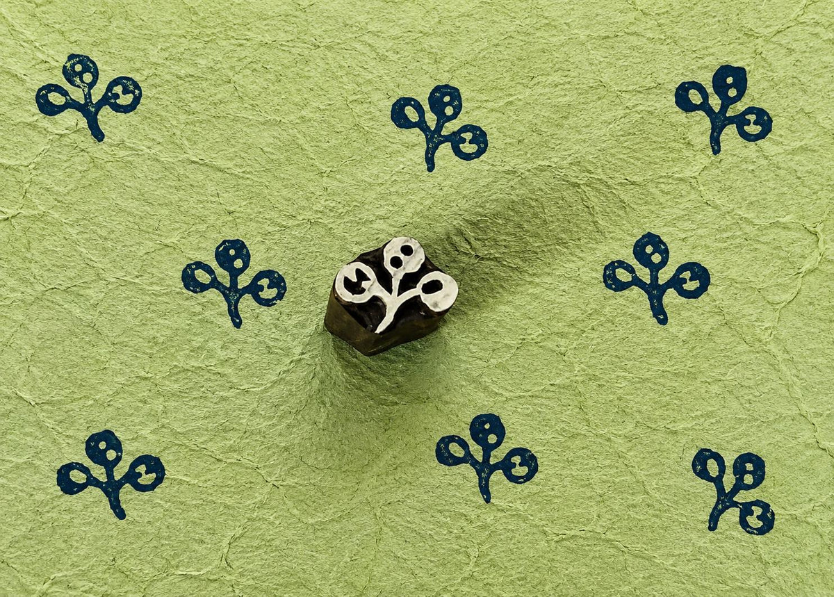 Tiny hand carved berry sprig wooden printing block stamped in navy blue ink on handmade green paper for textile printing, journaling, and folk art crafts.