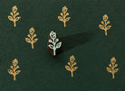Tiny hand carved wooden block stamp with stylized folk bud sprig motif printed repeatedly on dark textured handmade paper.