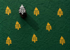 Tiny hand carved wooden evergreen tree block stamp printing repeating pine tree motif in golden yellow ink on textured forest green paper
