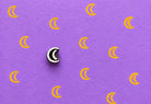 Tiny hand carved wooden crescent moon block stamp printing repeating moon motifs in golden yellow ink on textured lavender paper