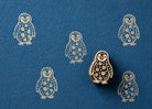 Hand carved penguin wooden stamp creating repeating cream colored prints on textured blue handmade paper.
