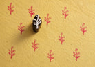 Hand carved wooden printing block with a tiny coral sprig design creating repeating pink impressions on textured handmade paper.