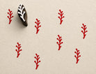 Tiny hand carved berry stem block stamp with repeating red botanical branch impressions on textured paper
