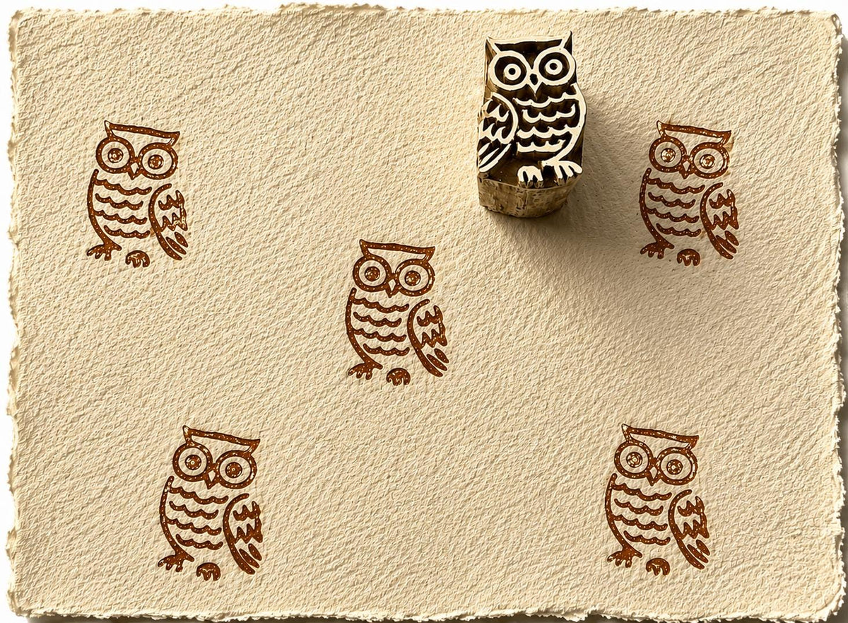 Hand carved wooden owl printing block creating repeating brown owl impressions on textured handmade paper.