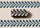 Hand carved wooden border block stamp printing repeating leafy vine border in deep blue ink on textured handmade paper