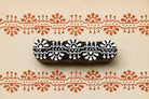 Hand carved wooden border printing block featuring repeating sunburst and geometric folk motifs stamped in terracotta ink on handmade paper.
