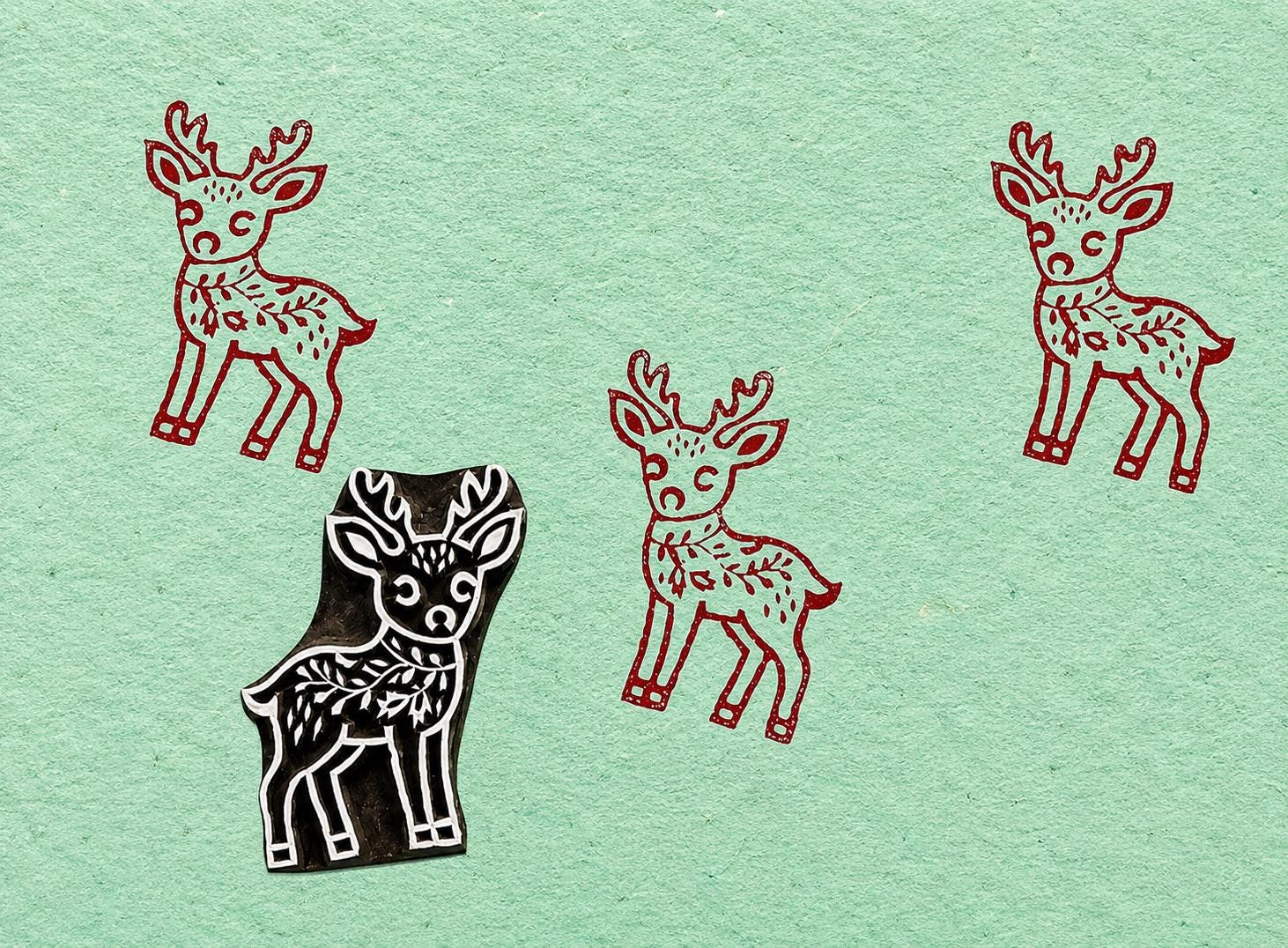 Hand carved deer printing block shown with repeating red deer impressions on handmade mint green paper.