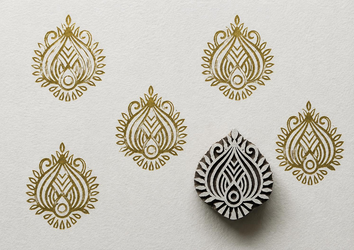 Hand carved wooden lotus flame printing block displayed with repeating gold lotus motif impressions on textured white paper.