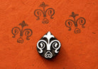 Small hand carved wooden floral motif block stamp printing repeating fleur inspired folk pattern on textured terracotta paper