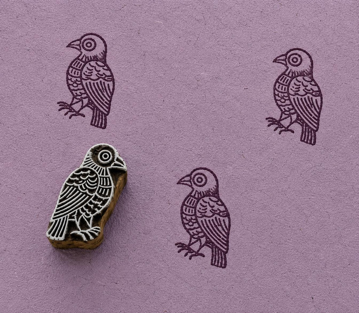 Hand carved folk songbird stamp creating plum coloured impressions on textured handmade paper.