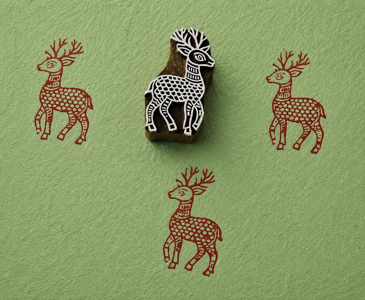 Hand carved wooden stag printing block with folk-art deer impressions on green handmade paper.