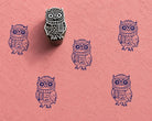 Hand carved wooden owl block stamp with winter scarf design and blue impressions on textured pink handmade paper